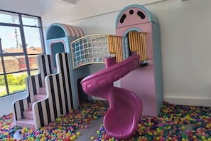 Zona de juegos infantiles con tobogán, estructuras de escalada y piscina de pelotas.