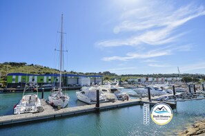 A marina with several yachts docked at the pier, a green building with a blue roof, and a clear blue sky. - ID #6 BnB Homes Apartment T1 Encosta Da Orada Complex (Albufeira)