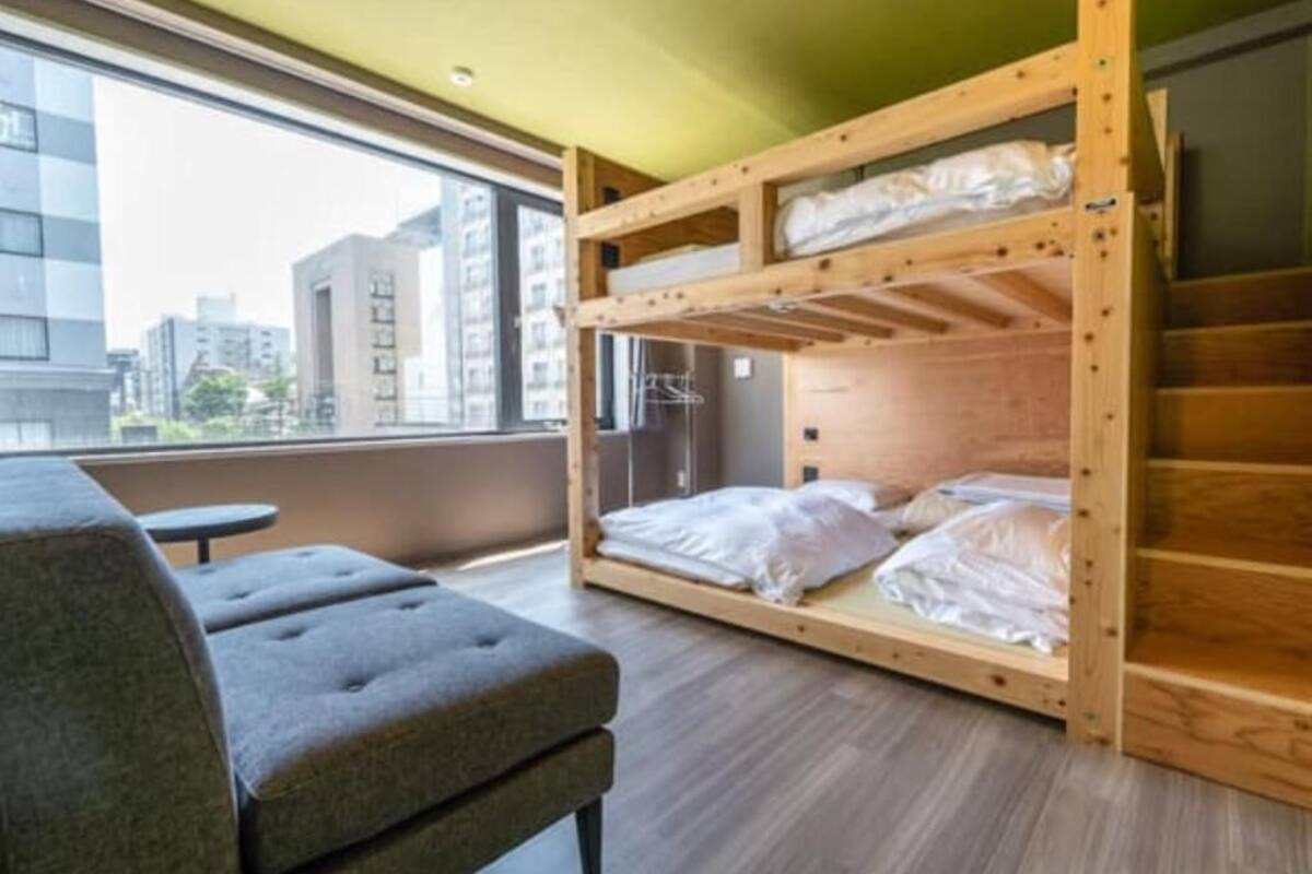 A bunk bed with a view of buildings through a window, a grey sofa, and a small table.