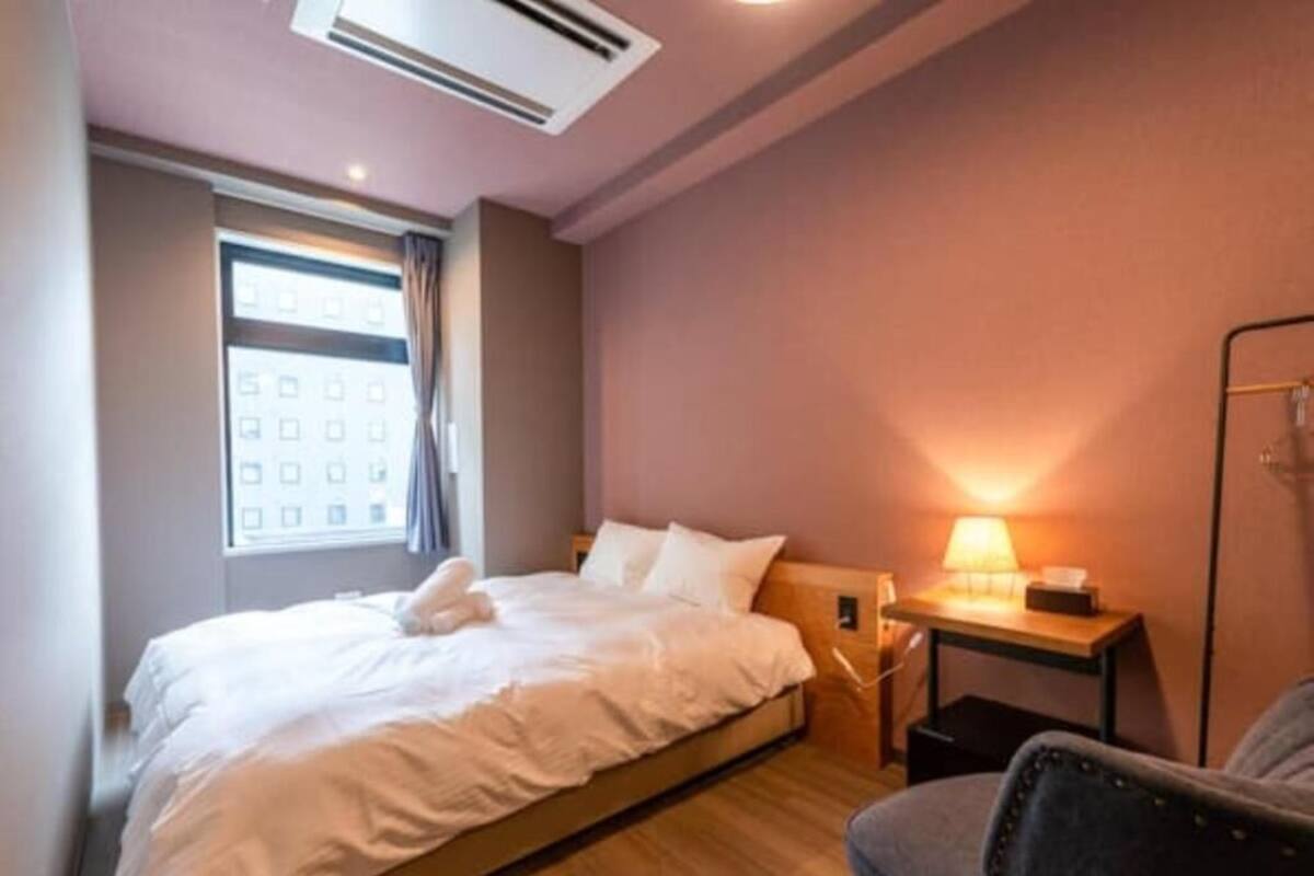 A hotel room with a bed, a desk with a lamp, a chair, and a window with curtains.