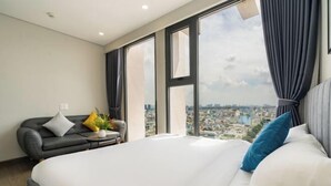 Une chambre d’hôtel avec un grand lit, un canapé, une petite table avec une plante et une vue sur la ville à travers de grandes fenêtres.