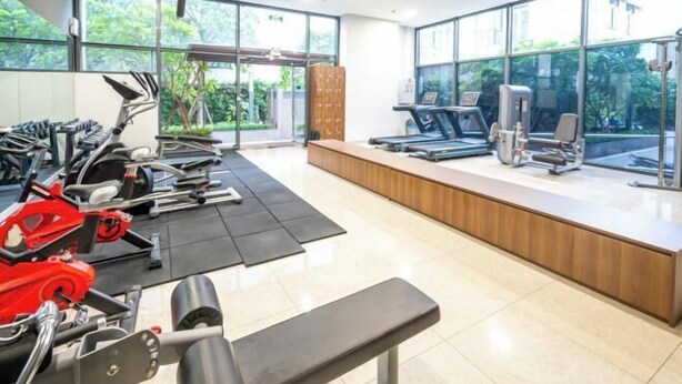 Une salle de sport équipée de matériel d’exercice, d’un banc et de grandes fenêtres donnant sur un espace verdoyant.