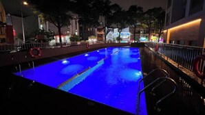 Une piscine nocturne éclairée de lumières bleues, entourée d’une clôture et d’arbres.