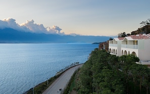 A coastal hotel with a view of the sea and mountains in the background.