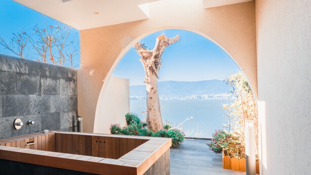 A modern bathroom with a large bathtub, a stone wall, and a view of the sea.