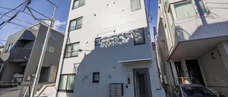 A multi-story residential building with a flat facade, a car parked in front, and visible electrical wires overhead.