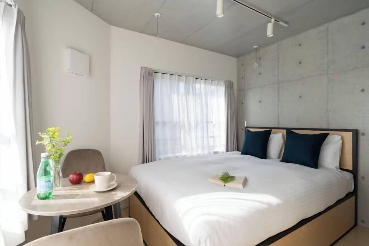 Une chambre d’hôtel avec un lit, une petite table sur laquelle se trouvent une bouteille, une pomme et une tasse.