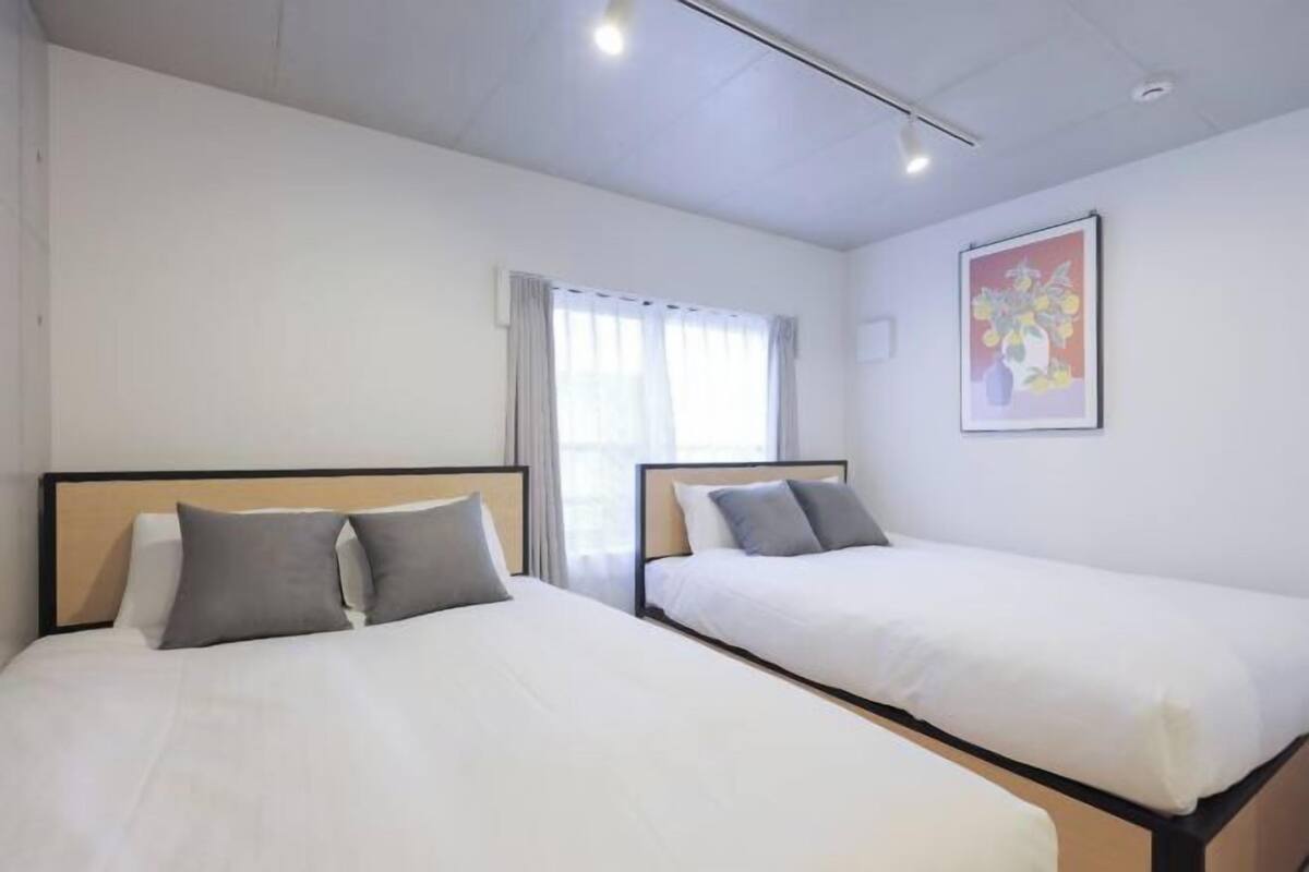 A hotel room with two beds, a window with curtains, and a framed picture on the wall.