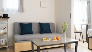A modern living room with a grey sofa, two dark blue cushions, a coffee table with fruits and a book, and a plant. - Bel Avenir (Tokyo)