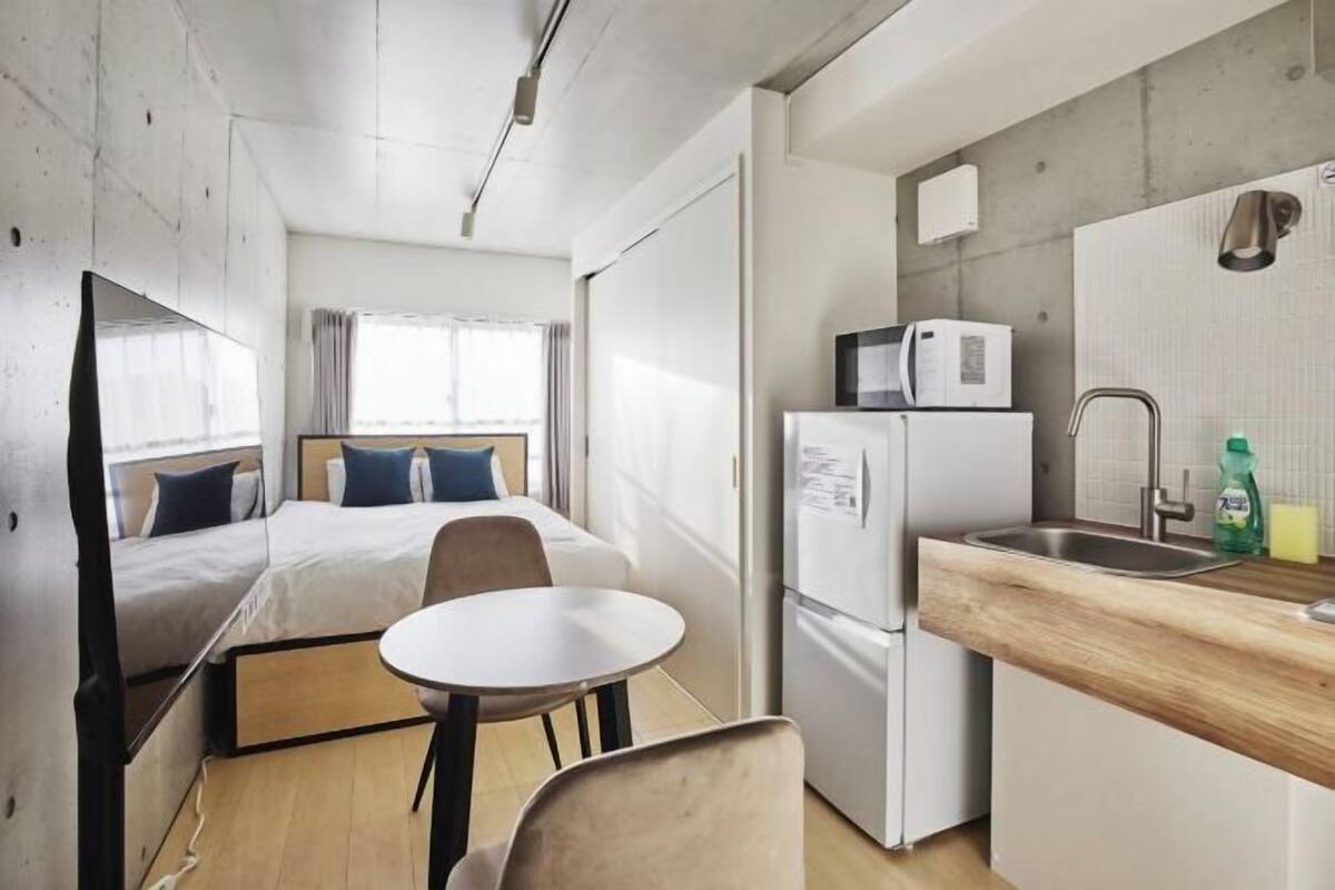 A compact room with a bed, a small table, a sink, and a microwave.