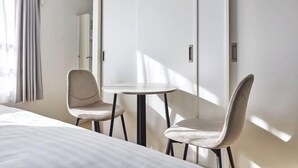 A hotel room with a bed, two chairs, a small round table, and a wardrobe. - Bel Avenir (Tokyo)