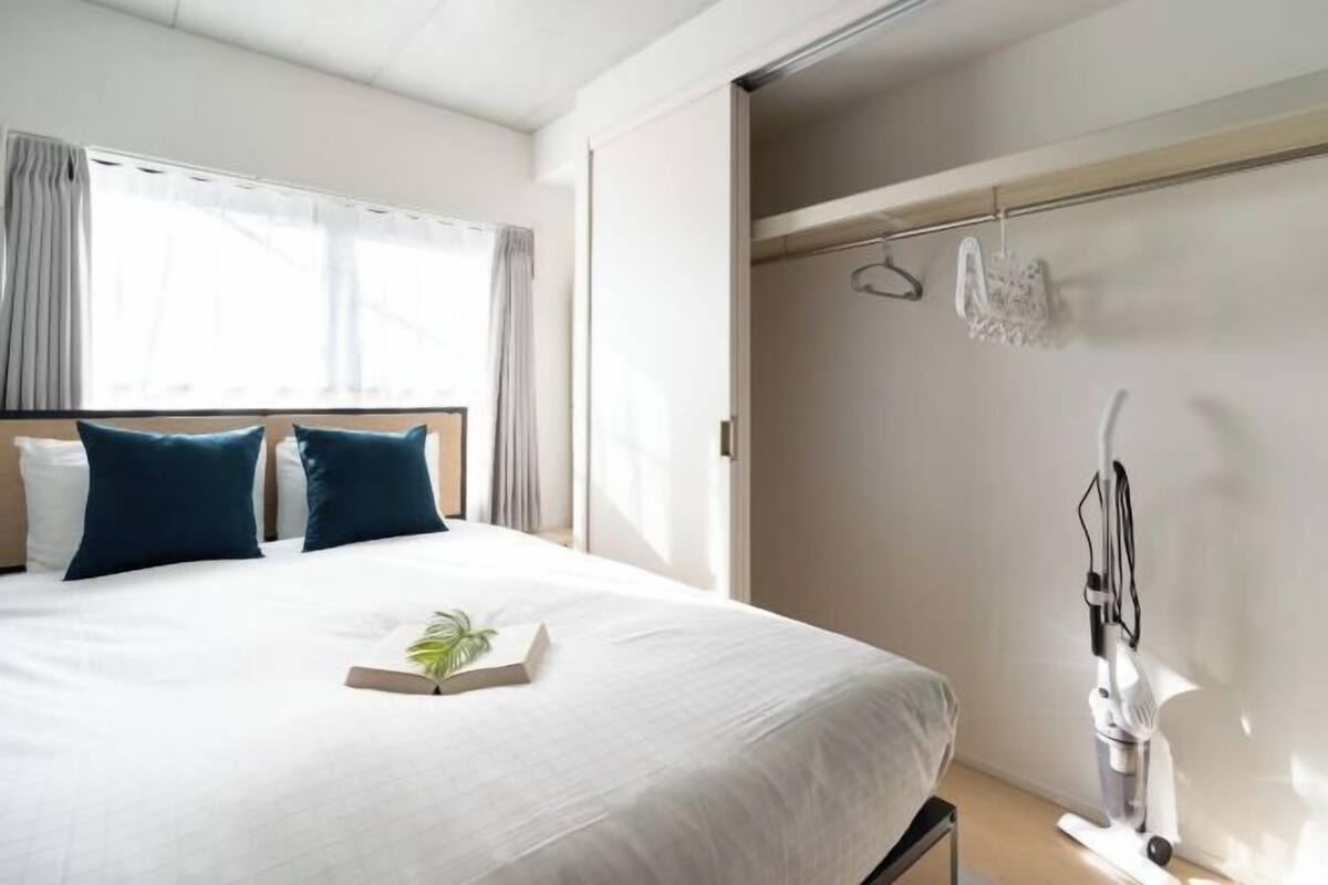 A modern hotel room with a large bed, a bedside table with a plant, and a vacuum cleaner against the wall.