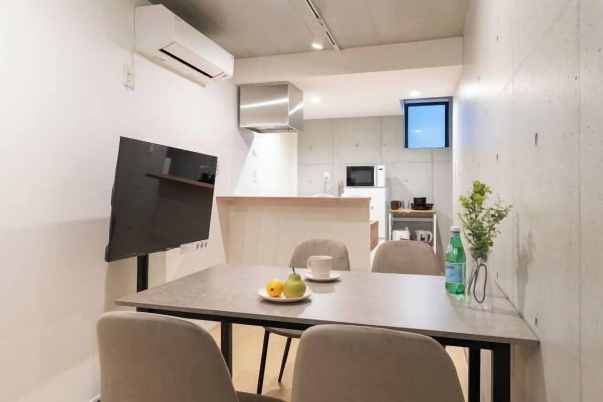 A modern kitchen with a flat-screen TV, a dining table with chairs, and a small plant on the table.