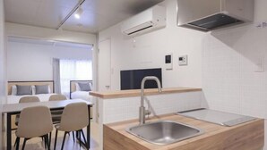A compact hotel room with a kitchenette, a dining area, and a bed with a headboard. - Bel Avenir (Tokyo)