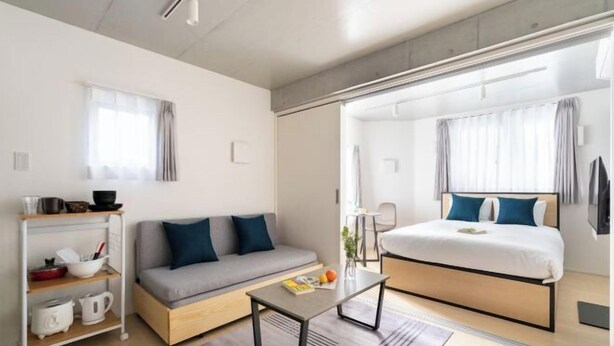 A modern hotel room with a sofa, a bed, a small table, and a kitchenette area. - Bel Avenir (Tokyo)