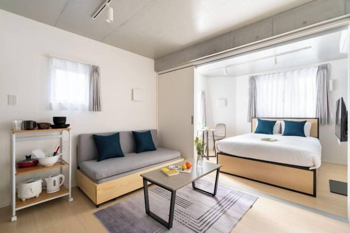 A modern hotel room with a sofa, a bed, a small table, and a kitchenette area.