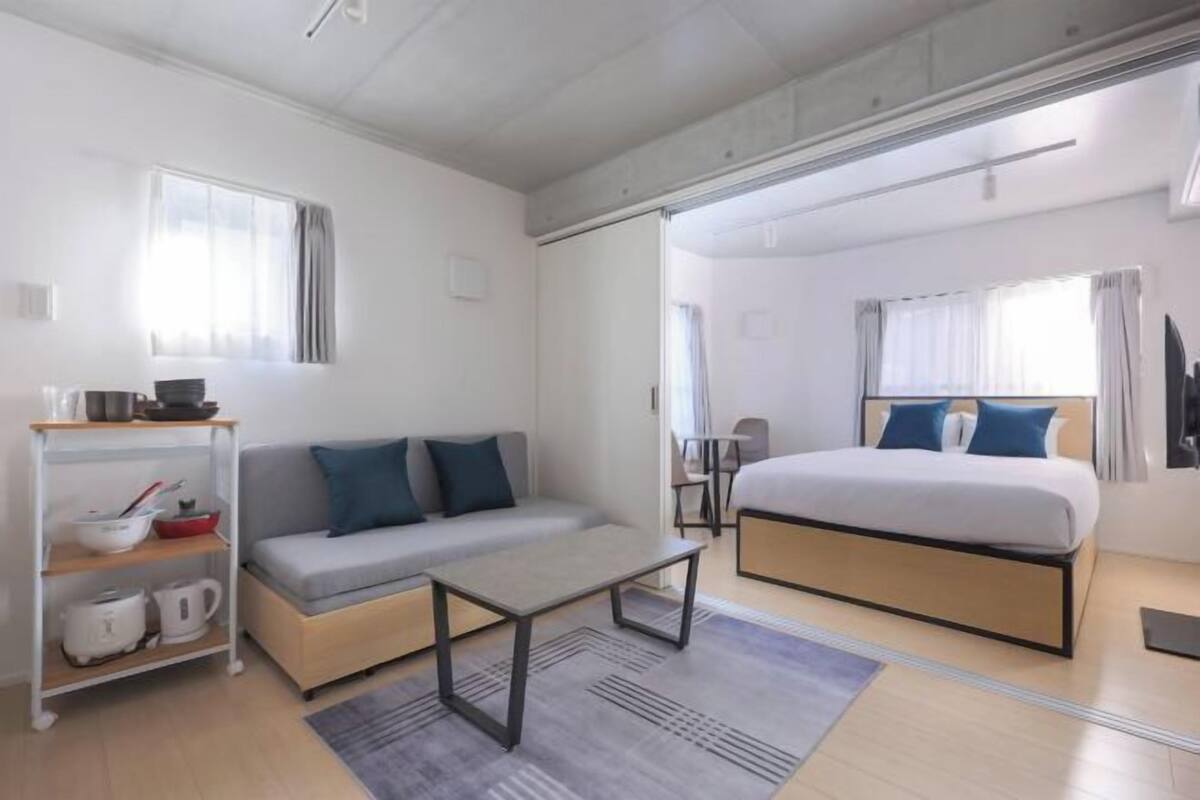 A modern hotel room with a sofa, a bed, a small table, and a kitchenette area.