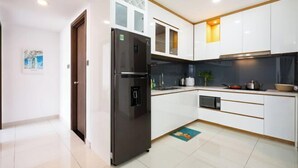 A modern kitchen with white cabinets, a black refrigerator, and a microwave. - Saigon Royal and Tresor apartments (Ho Chi Minh City)