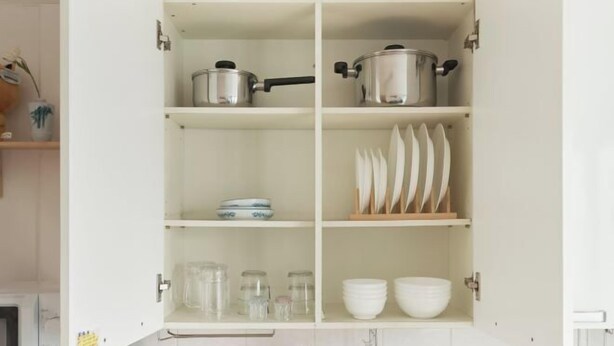 Una cocina con armarios blancos, ollas de acero inoxidable, frascos de vidrio y vajilla blanca.