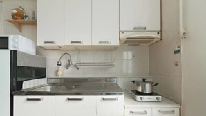 Una cocina compacta con armarios blancos, un lavamanos de acero inoxidable, un microondas y una estufa a gas.