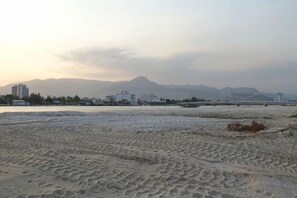 Una playa con dibujos en la arena, una montaña a lo lejos y edificios al fondo.