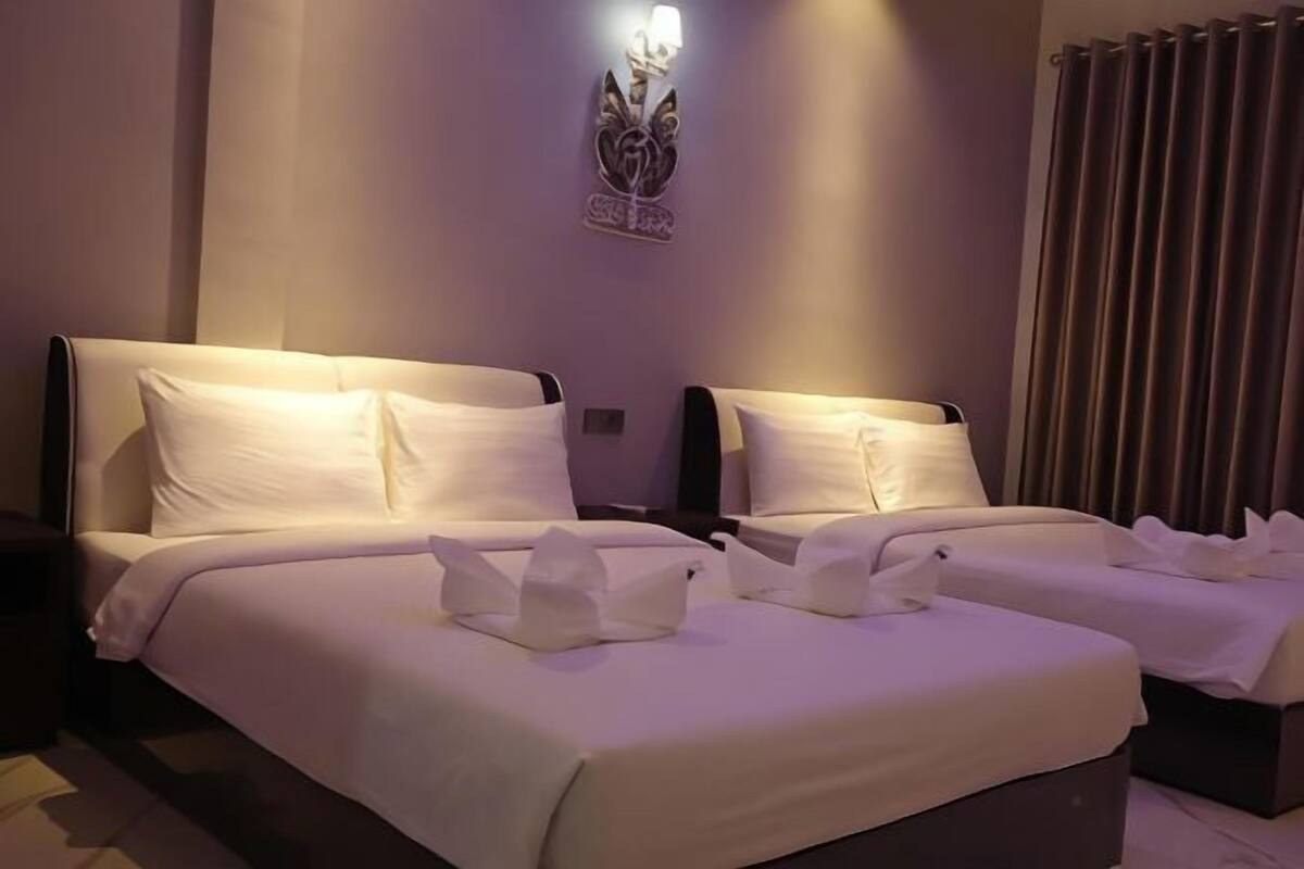 A hotel room with two beds, each with white linens and pillows, a wall-mounted light fixture, and a curtain on the window.