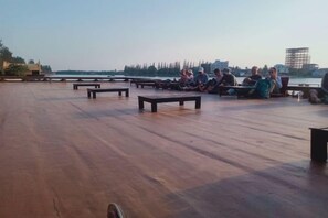 Una terraza de madera al aire libre con bancos y gente sentada.