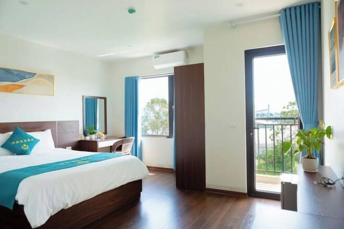 Une chambre d’hôtel comprenant un lit, un bureau, une chaise, une fenêtre avec des rideaux et un balcon.