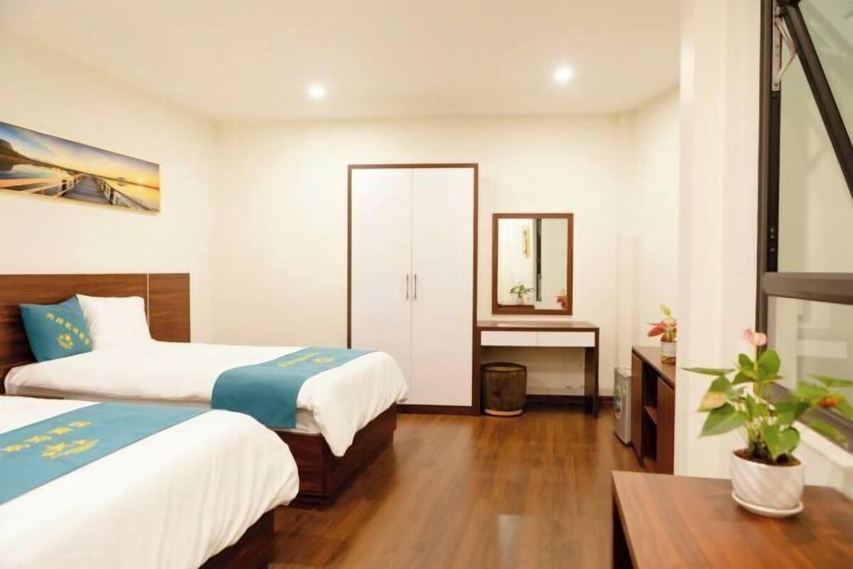 Une chambre d’hôtel avec deux lits, un bureau, un miroir, une poubelle et une fenêtre.