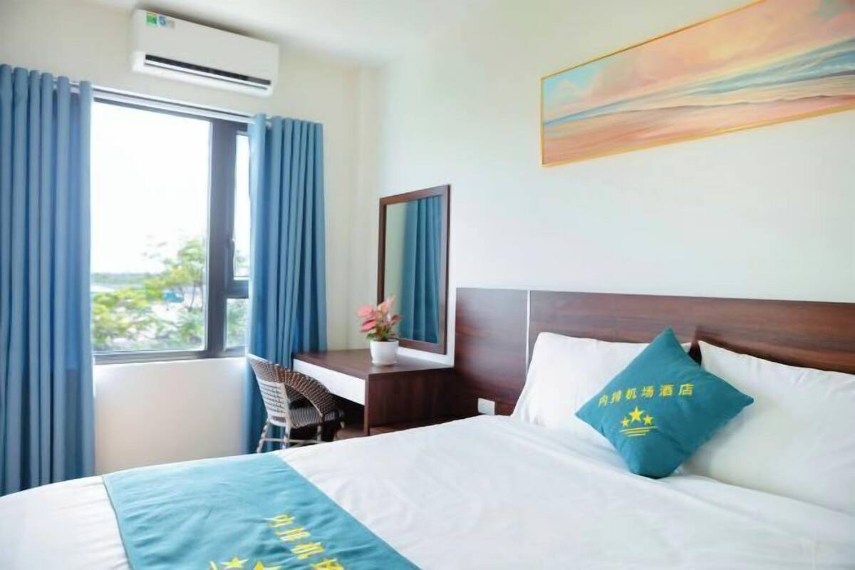 Une chambre d’hôtel avec un lit, un bureau et une chaise, une fenêtre avec des rideaux, un climatiseur et un tableau au mur.