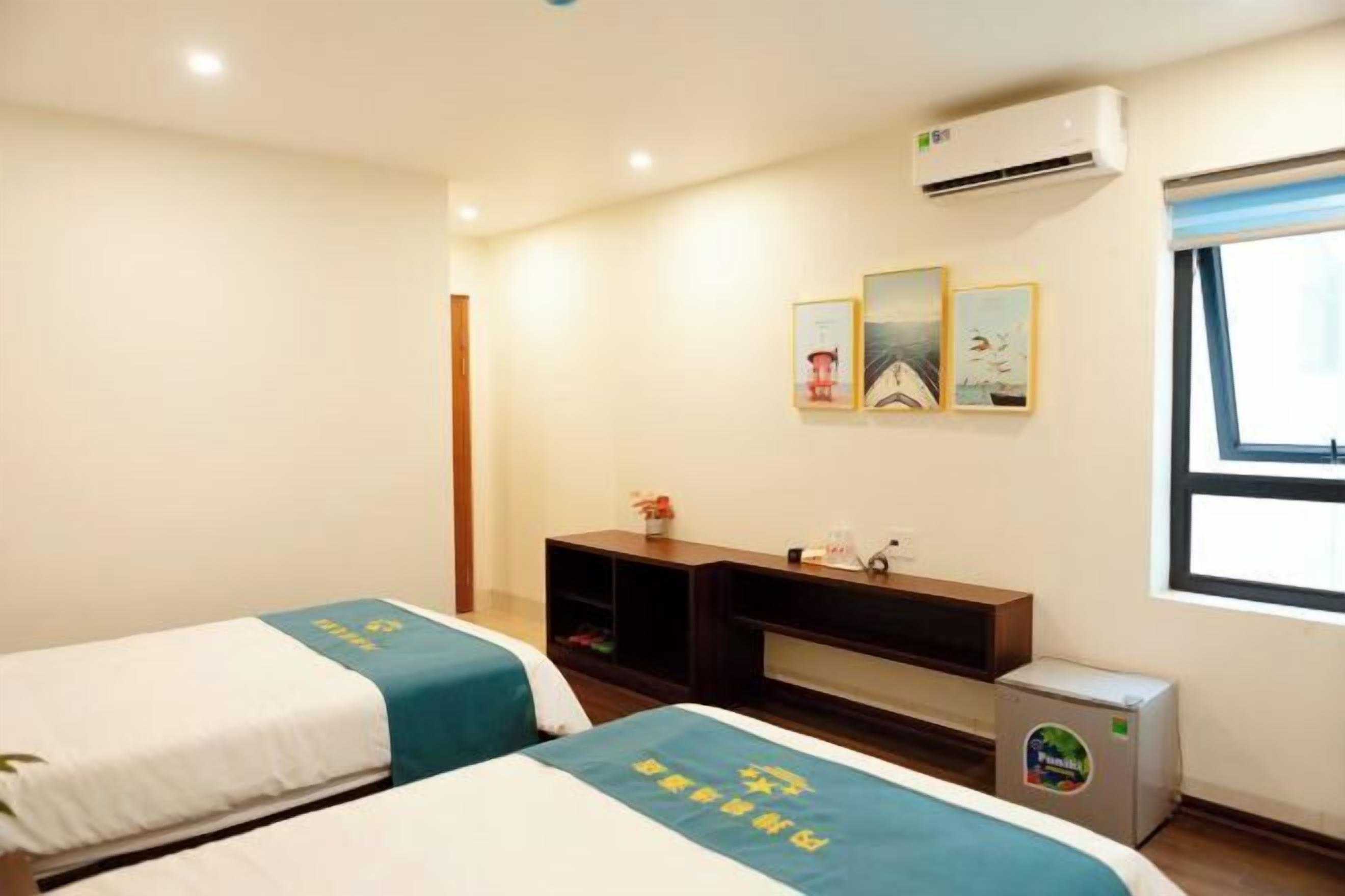Quarto de hotel com duas camas, uma televisão pequena, um mini-refrigerador e uma janela com persianas.