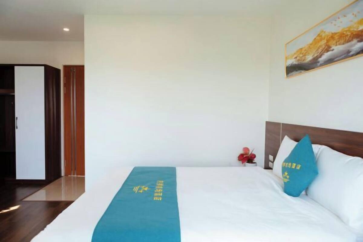 Une chambre d’hôtel avec un lit, un couvre-lit bleu orné d’un motif textuel, un tableau au mur et une tête de lit en bois.