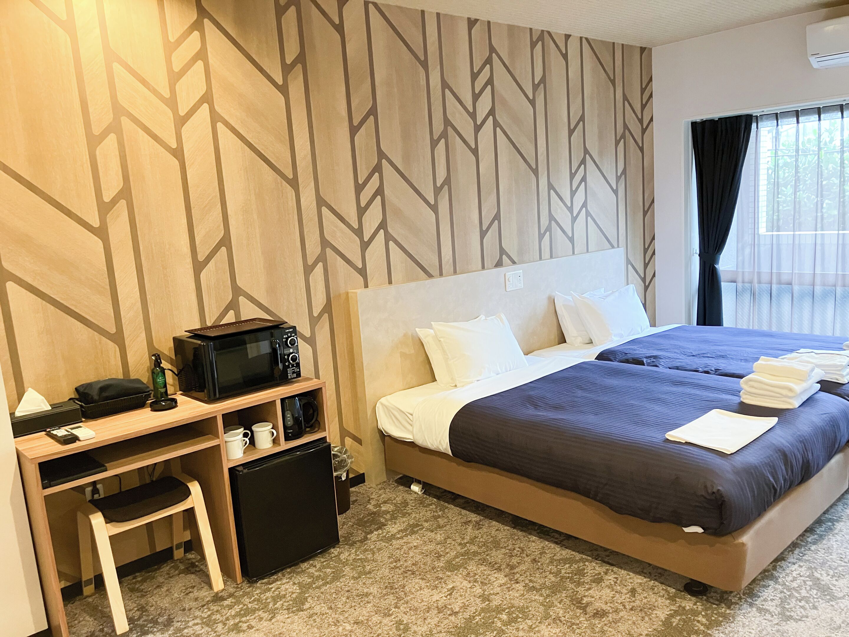 A hotel room with a bed, a desk with a microwave, a small refrigerator, and a chair.