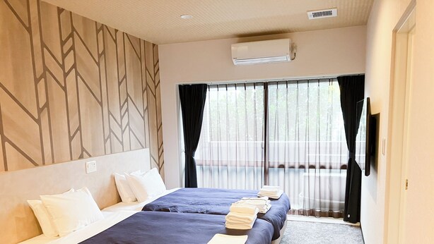 A hotel room with two beds, a large window with curtains, an air conditioning unit, and a patterned wall. - HOTEL LiVEMAX Naha Naminoue II (Naha)