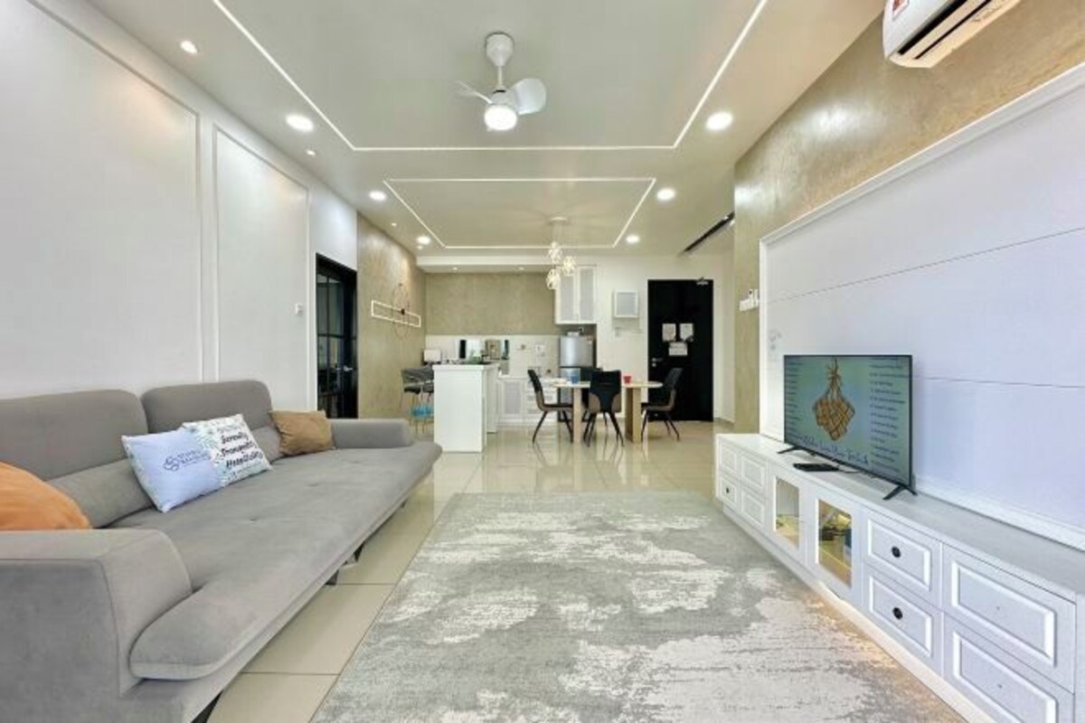 A modern living room with a grey sofa, a flat-screen TV, and a dining area with chairs and a table.