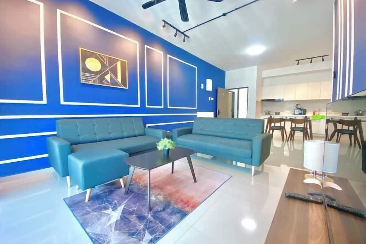 Uma sala de estar moderna com um sofá seccional, uma mesa de centro e uma cozinha ao fundo.