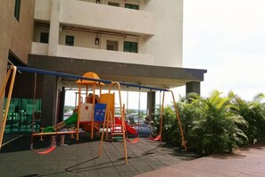 An outdoor play area with swings and slides, located in front of a building with a covered entrance. - PD D’Wharf Amazing Seaview Suite 9 (Up to 6 Pax) (Port Dickson)