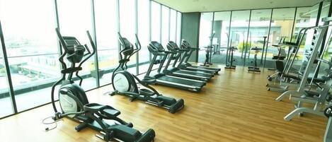 A gym with cardio equipment, large windows, and a wooden floor.
