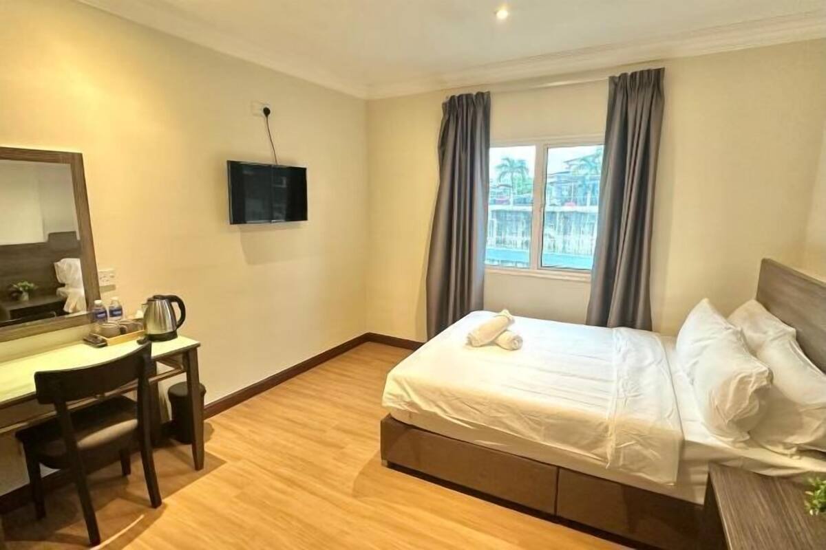 A hotel room with a bed, a desk, a chair, a television, and a window with curtains.