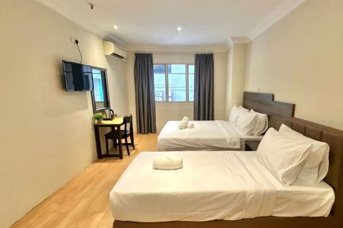 A hotel room with two beds, a desk, a chair, a TV, and a window with curtains.