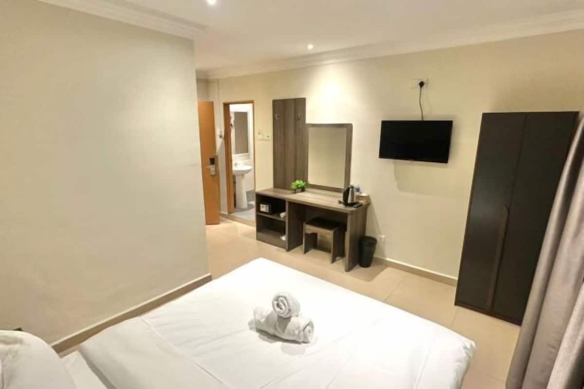 A hotel room with a bed, a desk, a mirror, and a TV.