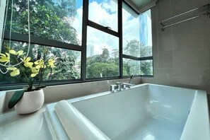 Une salle de bain moderne avec une grande baignoire, une plante en pot et une vue sur la verdure grâce à de grandes fenêtres.