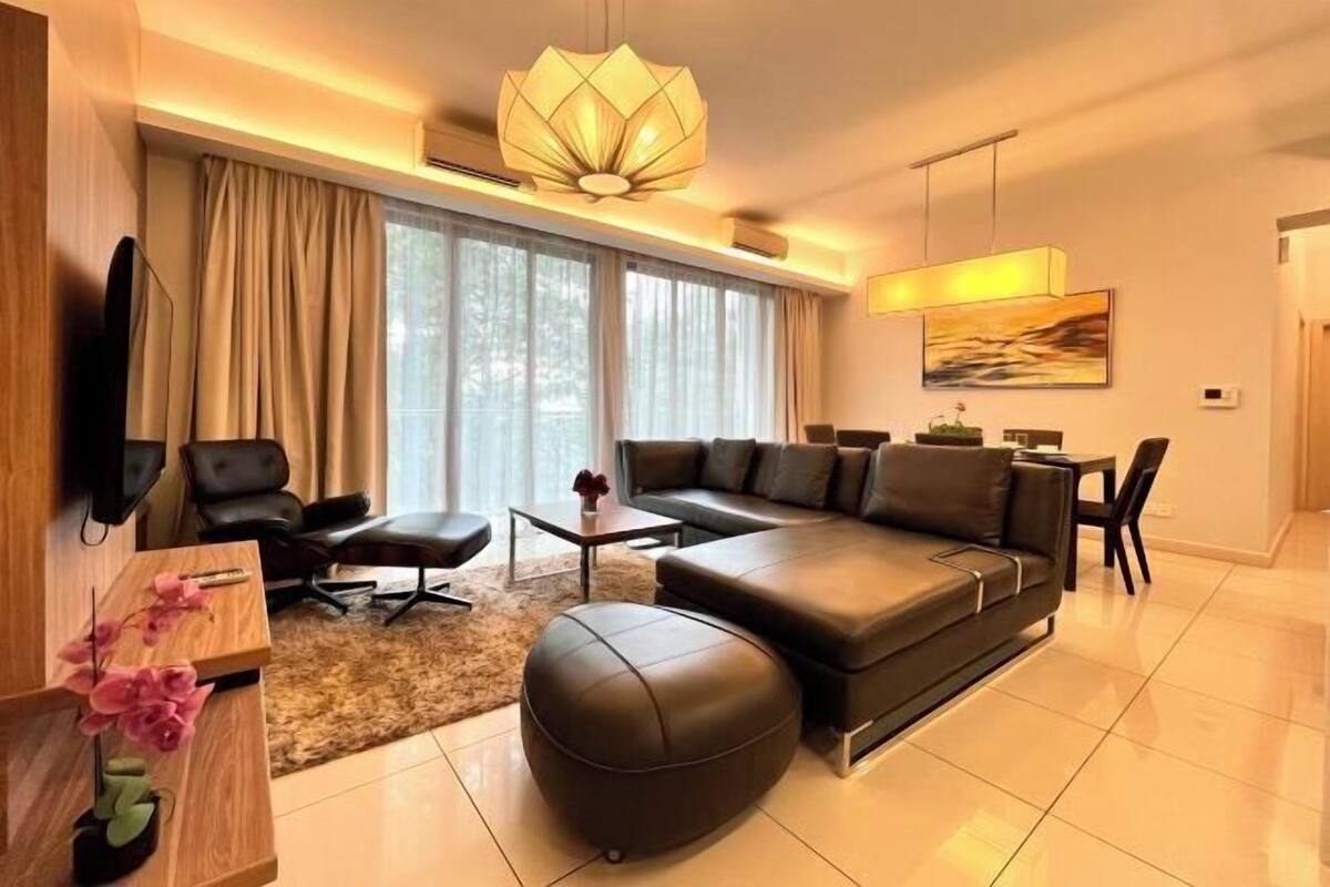 Un salon moderne avec un canapé, un pouf et un téléviseur posé sur un meuble en bois.