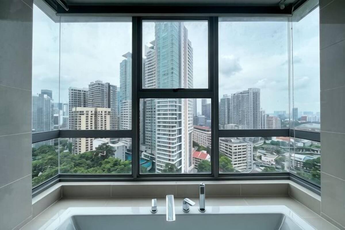 Une salle de bain dotée d’une grande fenêtre, d’une baignoire et offrant une vue sur le paysage urbain.