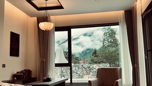 A modern living room with a large window, a stone wall, a sofa, a chair, and a hanging light fixture. - Mid Hill White Lodge (Ngawa Autonomous Prefecture)