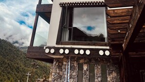 A multi-level wooden structure with a large window and a stone base, set against a mountainous backdrop. - Mid Hill White Lodge (Ngawa Autonomous Prefecture)