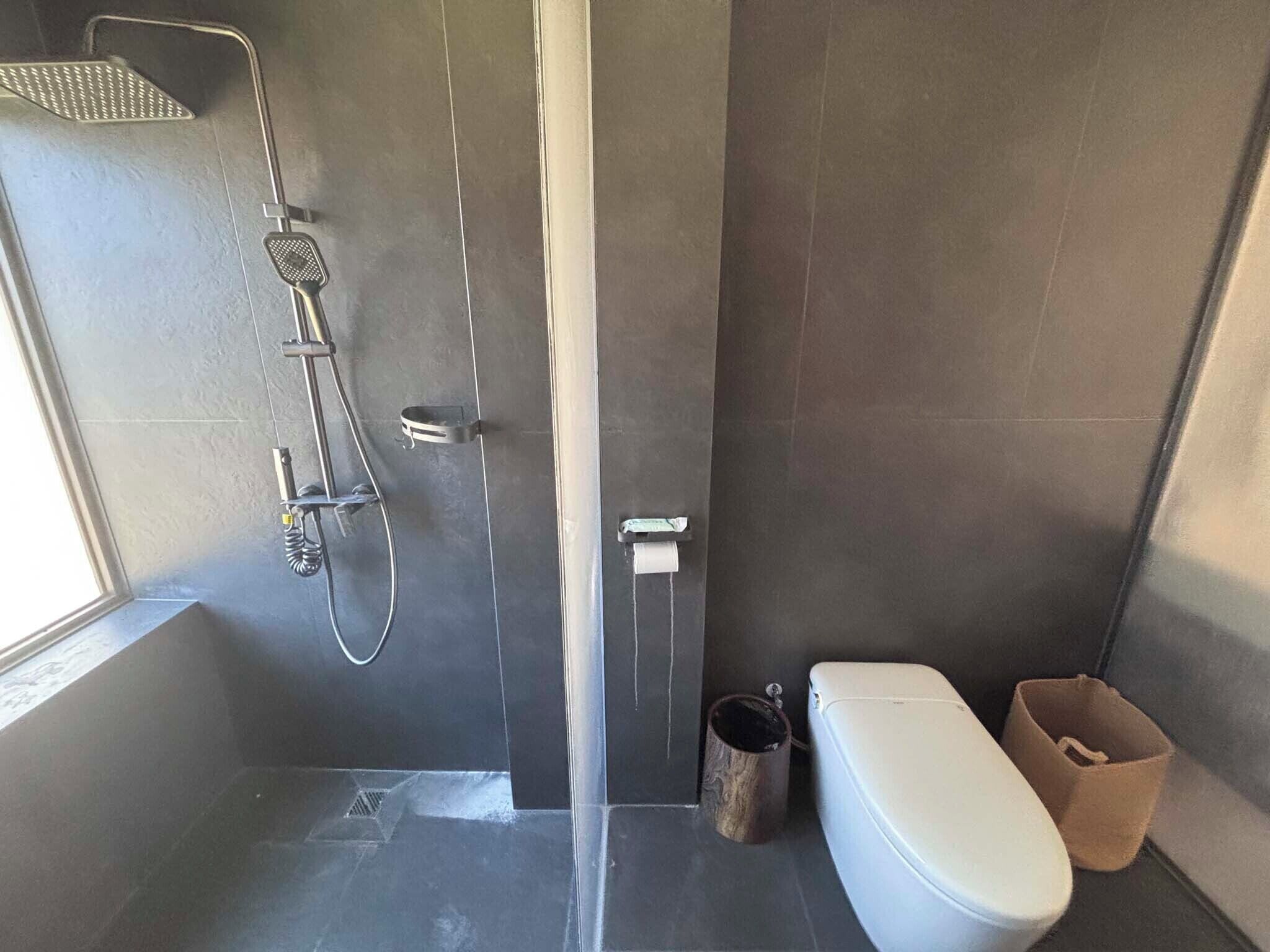 Un baño moderno con ducha, inodoro y un pequeño cubo de basura.