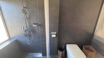 Un baño moderno con ducha, inodoro y un pequeño cubo de basura.