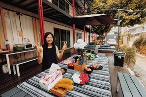 Un espacio de comedor al aire libre con una mesa dispuesta con comida, un cesto de basura y un banco.