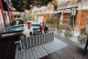 A couple sitting on a striped bench with a view of a courtyard and a building in the background. - SHIN Hostel Changphuak ChiangMai (Chiang Mai)